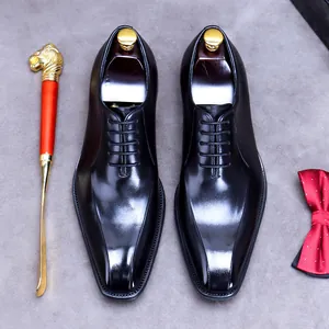 Classic black leather Oxford shoes with square toe, gold shoehorn and red bowtie on grey