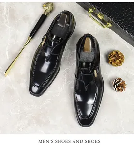 Detail of black patent leather monk strap shoe with gold buckle on marble background