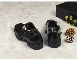 Polished black leather monk strap shoe with gold buckle detail on marble surface