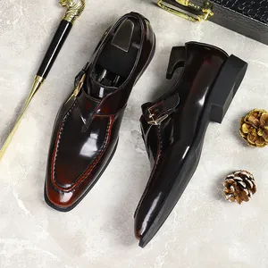 Formal men's burgundy glossy leather monk strap shoes with gold buckle on marble surface