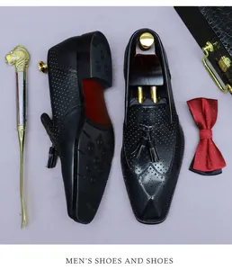 Dettaglio di scarpe brogue in pelle nera con nappe, calzante dorato e papillon rosso