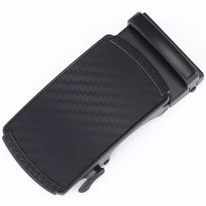 Close-up of black matte automatic belt buckle with carbon fiber texture and Greek key pattern