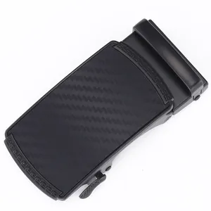 Detail of matte black automatic belt buckle with carbon fiber texture and Greek fret motif