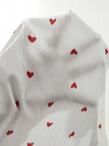 Gros plan sur un tissu blanc léger avec motifs cœurs rouges et texture tricotée