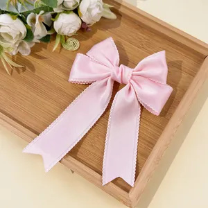 Detailed view of pink satin bow hairclip with lace edges and ribbons on wooden tray
