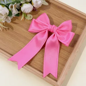 Detail of light pink satin bow hair clip with elegant serrated edges on a wooden tray