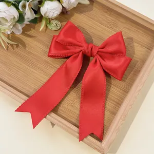 Detail of red bow hair clip with lace edges and long ribbons on a wooden tray