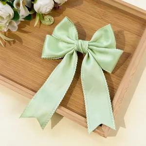 Detailed view of mint green satin bow hair clip with wavy edges and long streamers