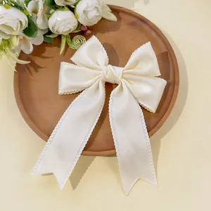 Detailed view of cream satin bow hair clip with decorative picot lace edges on wood