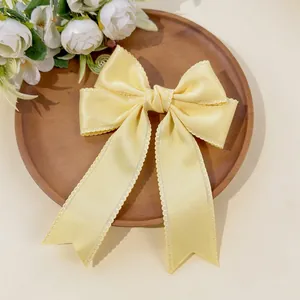 Detailed view of the yellow satin bow hair clip with elegant scalloped lace edges