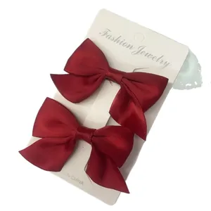 Pair of deep red satin bow hair clips for girls on a white jewelry display card