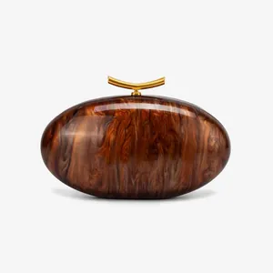 Detailed macro of acrylic shell clutch bag featuring amber marble texture and gold clasp