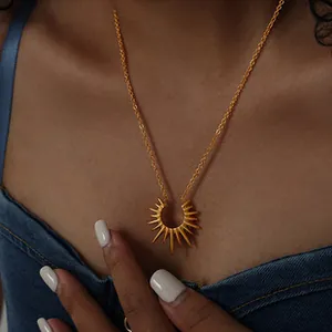 Detailed view of an 18K gold plated sunburst pendant necklace on a model wearing denim