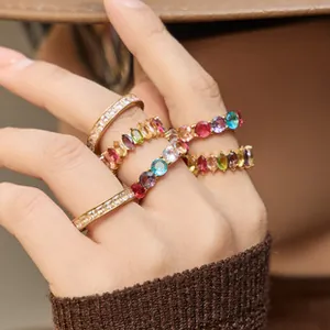 Close-up of gold-plated rings set with colorful crystals worn by a hand with knit cuff