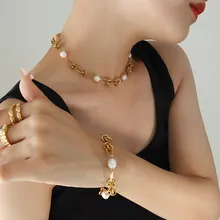 Close-up of chunky gold watch-strap chain necklace and white pearl bracelet on model