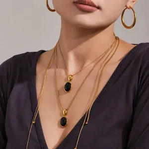 Détail d'un collier à double chaîne dorée avec pendentif ovale noir et créoles