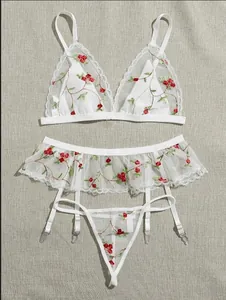 Detail of floral embroidery on white sheer mesh three-piece lingerie set with garters