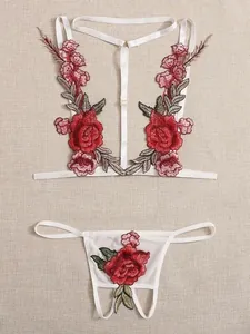 Détails d'un ensemble de lingerie blanche avec broderies florales rouges sur tissu beige