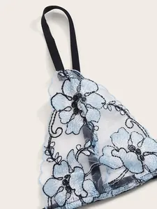 Close-up of white mesh lingerie set with blue floral embroidery and black elastic straps