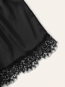 Detail of black satin fabric with delicate floral eyelash lace trim on the hemline
