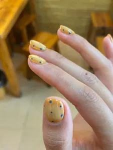 Detailed view of handmade oval press-on nails with yellow base and blue polka dot patterns