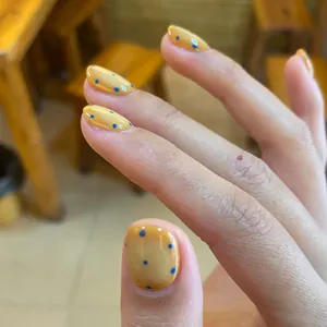 Short press-on nails with blue hand-painted dots on amber yellow translucent base