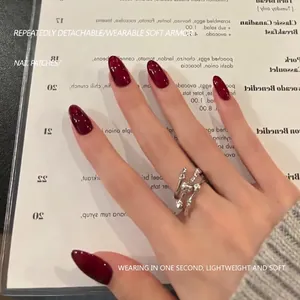 Glossy almond-shaped wine red press-on nails shown on hand with a silver textured ring