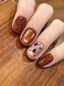 Dettaglio di unghie leopardate ambrate e cat-eye in calde tonalità marrone su legno