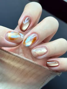 Detalle de uñas postizas ámbar jaspeado con efecto ojo de gato dorado y puntos marrones