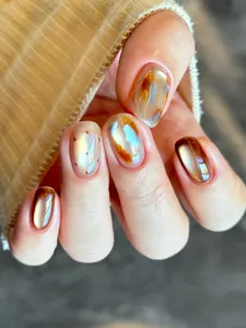 Primer plano de uñas postizas ámbar ojo de gato y jaspeadas azul-naranja con acabado brillo