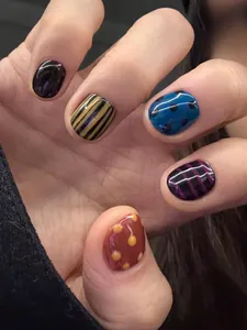 Close-up of short round press-on nails featuring red dots and striped patterns