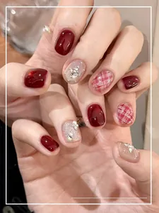 Detail of wine red press-on nails with silver glitter, pearls and plaid patterns