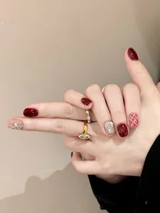 Detail view of wine red press-on nails with pearls, glitter, and grid patterns on hand