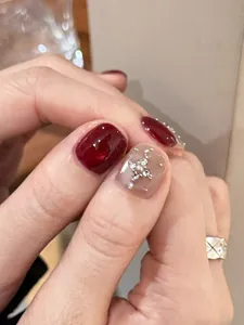 Detail of burgundy cat-eye press-on nails with silver cross accents and nude base color
