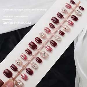 Short wine red press-on nails set with glitter, plaid patterns, and diamond cross accents