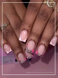 Dettaglio di unghie finte French rosa con accenti floreali 3D e strass scintillanti