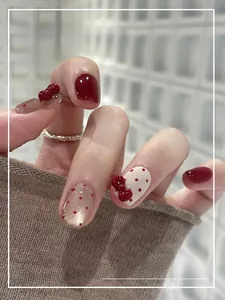 Detail of red wine press-on nails with white polka dots and a 3D ribbon bow ornament
