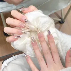 Dettaglio unghie finte fatte a mano con gemme viola, glitter e rilievi dorati 3D