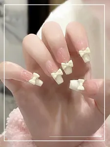 Detailed macro view of nude pink medium-long square press-on nails with white 3D bows