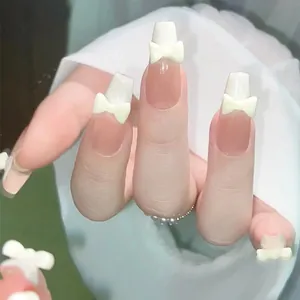 Close-up of nude pink French press-on nails with 3D yellow bows and white tips