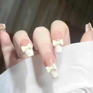 Close-up of nude press-on nails with white French tips and 3D resin bow accents