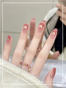 Détail de faux ongles dégradés roses avec des paillettes en cœur dorées brillantes