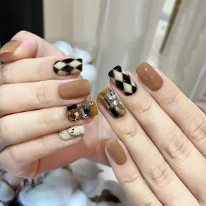 Macro shot of press-on nails featuring caramel plaid patterns and 3D rhinestone accents