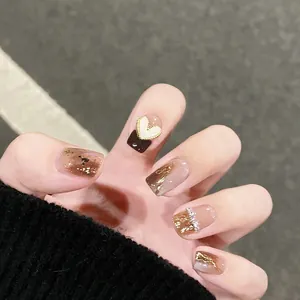 Detailed view of amber brown press-on nails with gold foil and heart-shaped 3D decor