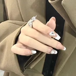 Detail of French white tip press-on nails with silver heart charms and a textured silver ring