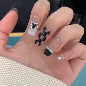 Detailed view of long coffin press-on nails with black checkered patterns and heart rhinestones
