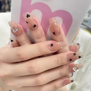 Close-up of nude press-on nails with black heart patterns and sparkling rhinestones