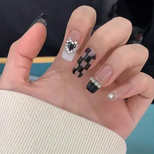 Close-up of handmade press-on nails with black heart rhinestones and checkerboard patterns
