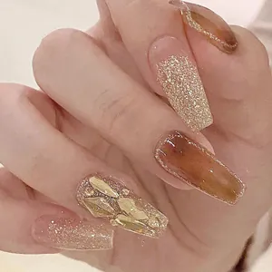 Macro detail of amber and champagne gold press-on nails with glitter and rhinestones