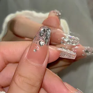Close-up of coffin nails featuring nude pink gradient, silver glitter, and 3D metal hearts
